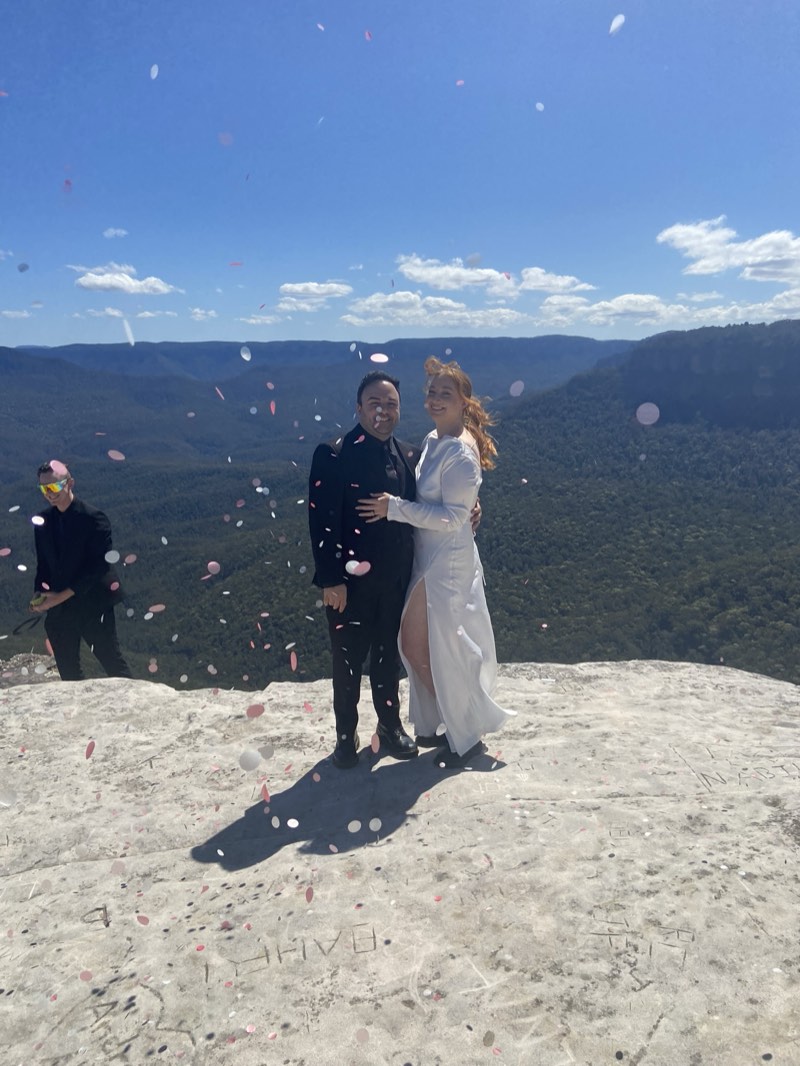 Petals thrown over a couple on a clifftop above the valley
