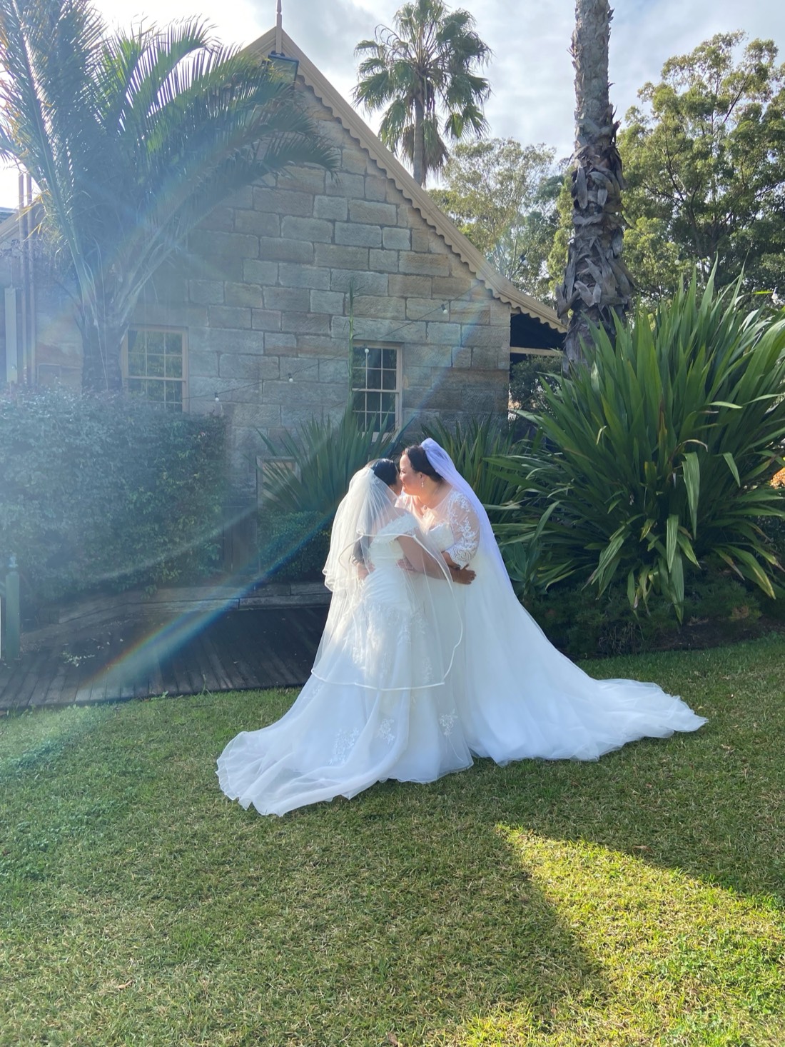 A bride with a long train on the lawn beside a sandstone chapel