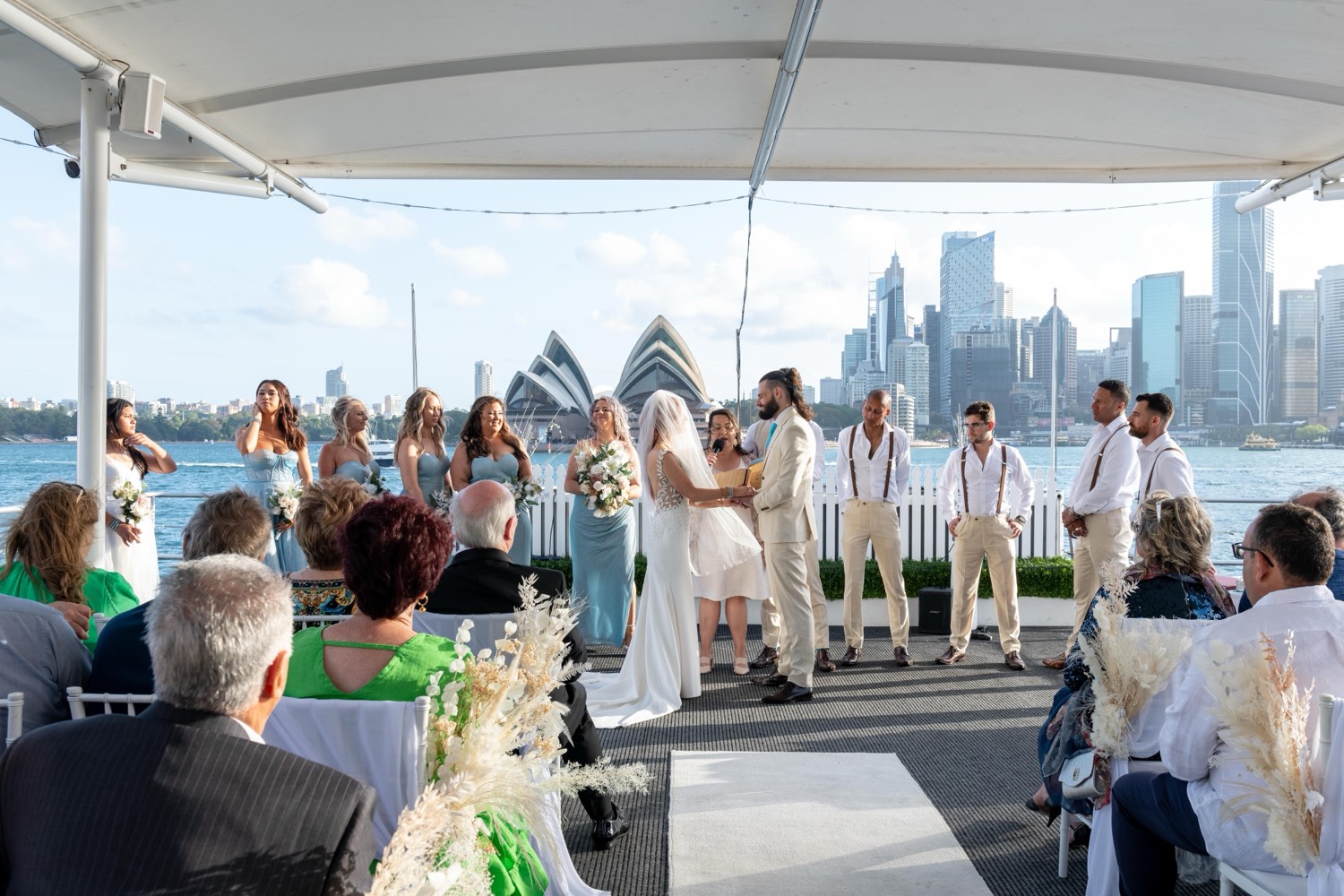 A wedding ceremony on a Sydney harbour lawn with the Opera House and city skyline behind