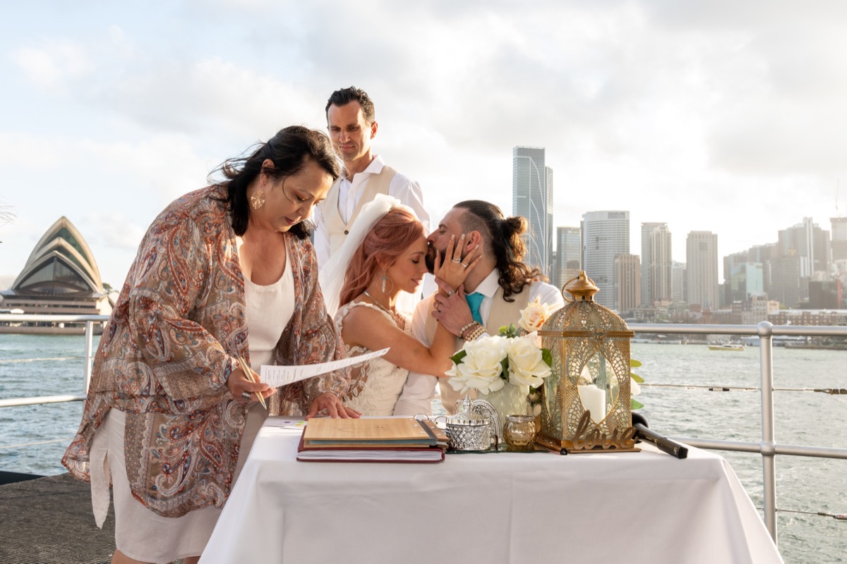 A couple signing the register on the harbour with the Opera House behind