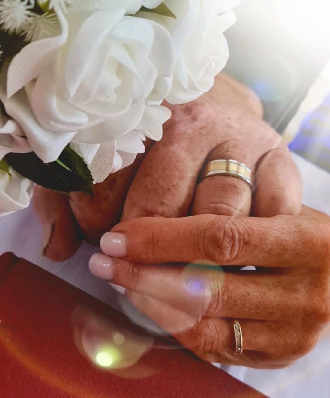 A couple's hands with their wedding rings, resting on white roses